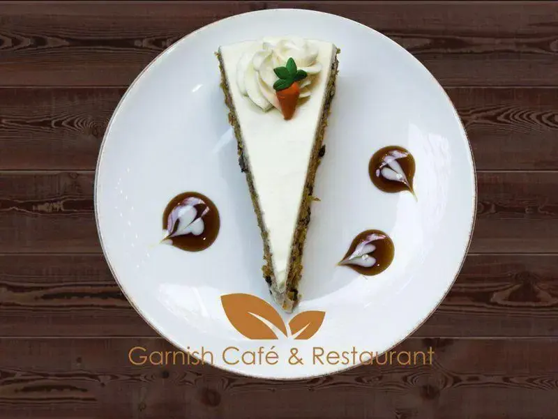 کیک هویج خوشمزه کافه رستوران گارنیش، با تزئینات زیبا روی بشقاب سفید، دسری عالی برای دوستداران شیرینی و قهوه.