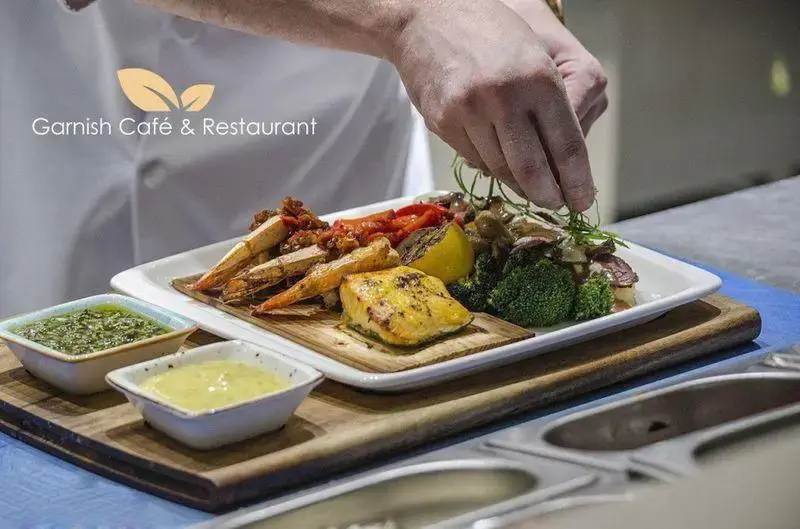 سرآشپز حرفه ای کافه رستوران گارنیش مشغول تزیین بشقاب غذای دریایی و سبزیجات تازه شامل ماهی سالمون، میگو و کلم بروکلی با دقت.