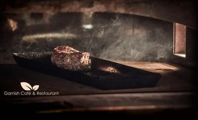 استیک گریل شده آبدار با دود خوش‌بو در محیط گرم فر کافه رستوران گارنیش، لذت طعمی بی‌نظیر.