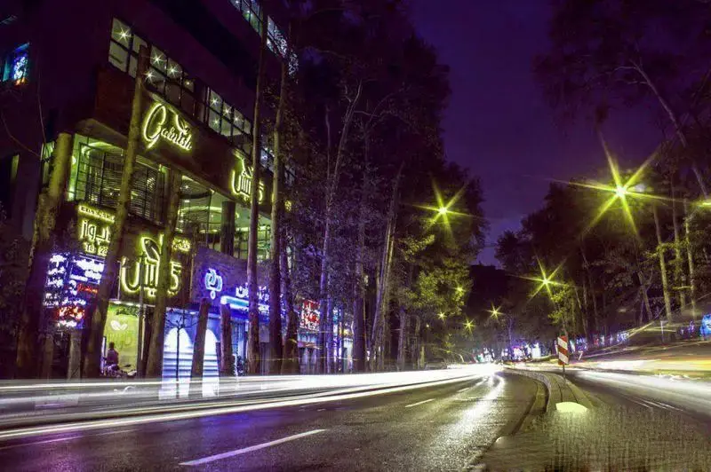 کافه رستوران گارنیش در شب، نمای بیرونی با نورپردازی درخشان، خیابان شلوغ و رد نور خودروها در فضایی دلپذیر.