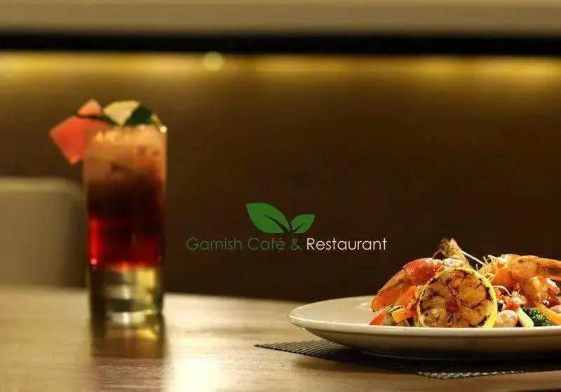 تصویری جذاب از نوشیدنی میوه‌ای لایه‌ای و بشقاب غذای دریایی لذیذ با میگو و لیمو گریل شده در کافه رستوران گارنیش.