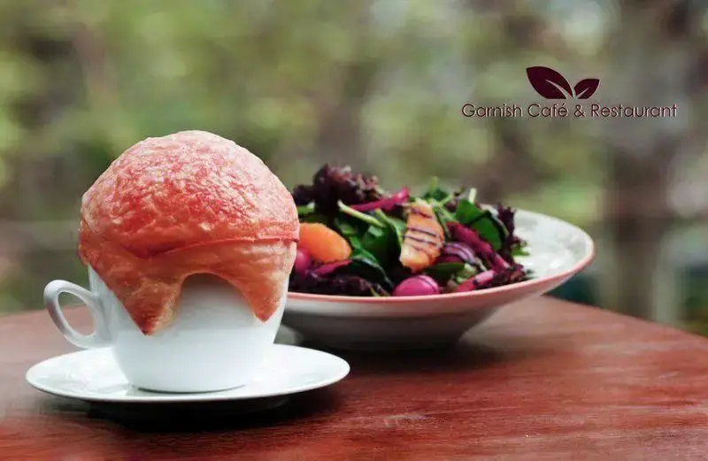 تصویری از سوپ پاف پاستری خاص کافه رستوران گارنیش در فنجان، در کنار سالاد فصل رنگارنگ، بر روی میز چوبی، پیشنهادی دلپذیر.