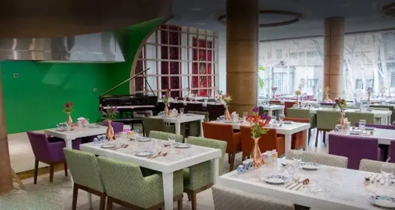 فضای داخلی دلباز کافه رستوران گارنیش با میزهای چیده شده، صندلی‌های رنگارنگ و پیانو، محیطی شیک و دلپذیر برای مشتریان.