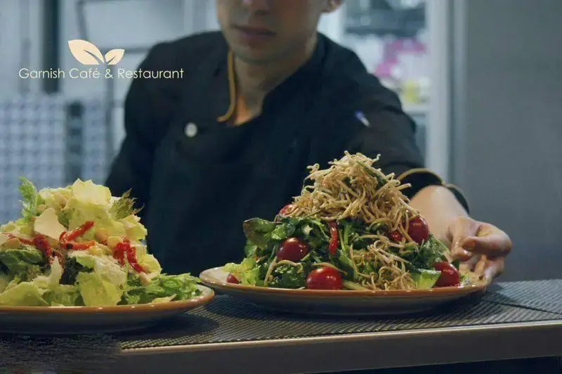 نمایی از سرآشپش کافه رستوران گارنیش در حال آماده‌سازی و سرو سالادهای تازه و رنگارنگ. تجربه غذای سالم و لذیذ در رستوران گارنیش.