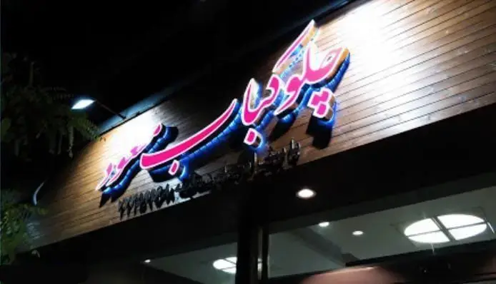 تابلو نئونی پیتزا و ساندویچ مسعود روی نمای چوبی رستوران مسعود در شب، جذب کننده نگاه مشتریان به این مکان.