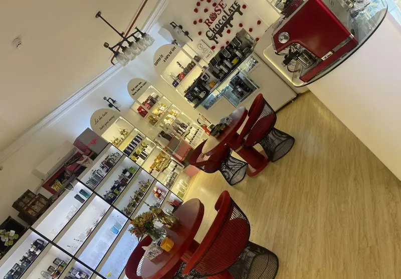 فروشگاه قهوه ننجون: فضای داخلی شیک با قفسه‌های نورانی پر از انواع قهوه، شکلات، لوازم خاص و هدایا، همراه با میز و صندلی‌های مدرن قرمز.