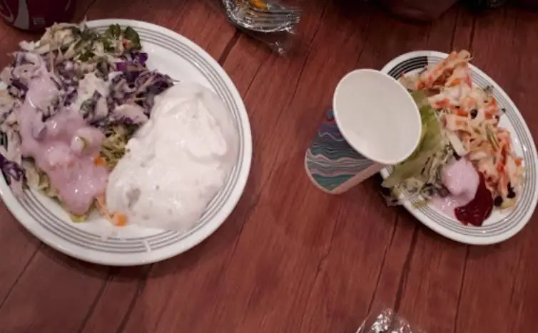 دو بشقاب پر از انواع سالادهای تازه و رنگارنگ رستوران سعادت روی میز چوبی. سالاد کلم، سالاد پاستا و سس‌های متنوع برای یک وعده غذایی سالم.