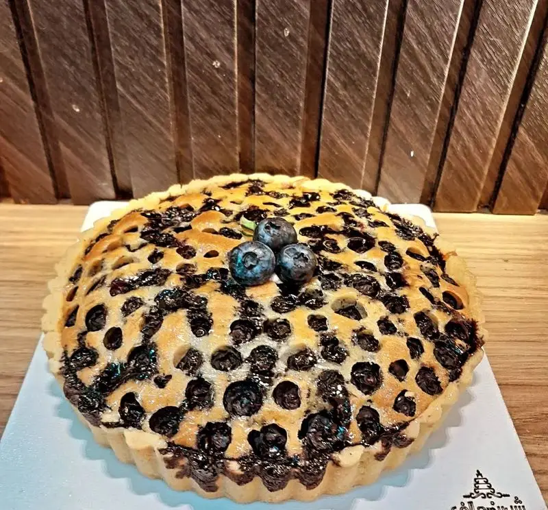 پای بلوبری تازه و دلپذیر شیرینی الف شعبه تهرانپارس، دسری شیک با بلوبری‌های آبدار و رویه حفره‌دار. ایده‌آل برای پذیرایی.