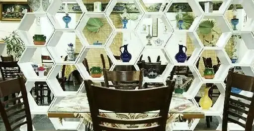 قفسه شش ضلعی سفید پر از دکوری‌های زیبا و گلدان در فضای زندگی بهشتی، مکانی آرام و دلنشین برای پذیرایی.