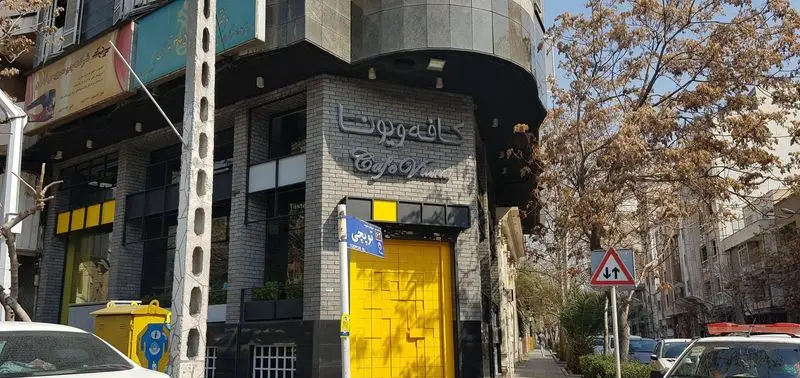 کافه ویونا با درب زرد رنگ و تابلوی روشن، نمایی از ورودی دنج و مدرن خود در یک روز آفتابی در خیابان‌های تهران را به نمایش می‌گذارد.