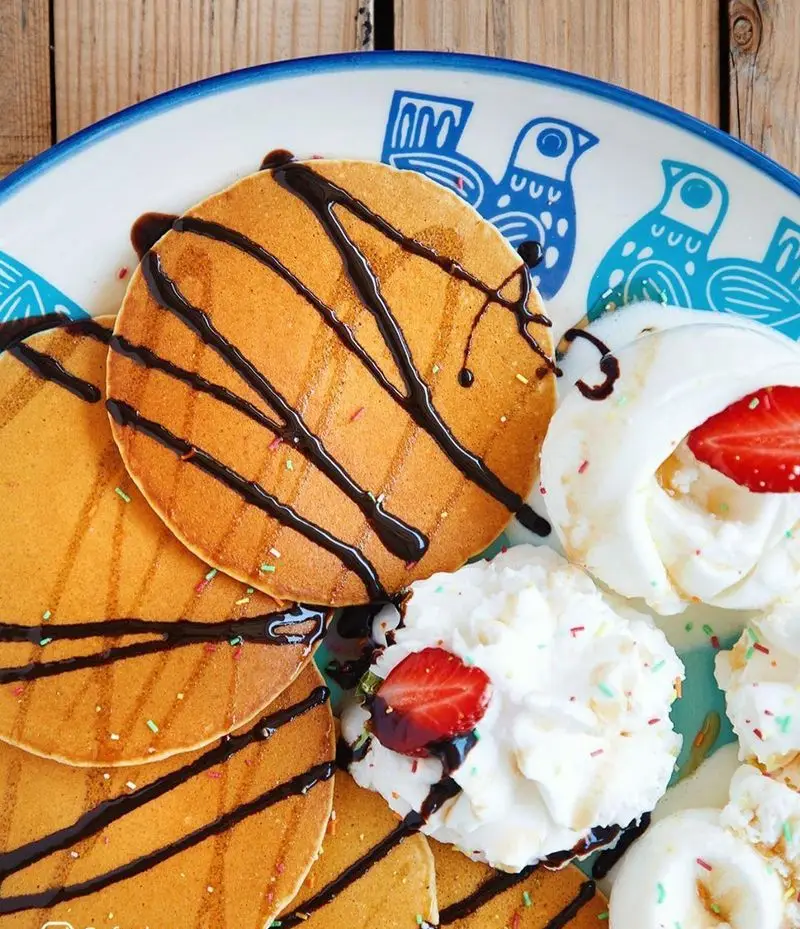 پنکیک‌های طلایی کافه شمرون با سس شکلات، توت فرنگی و خامه زده شده. ایده‌آل برای صبحانه یا دسر در تهران.