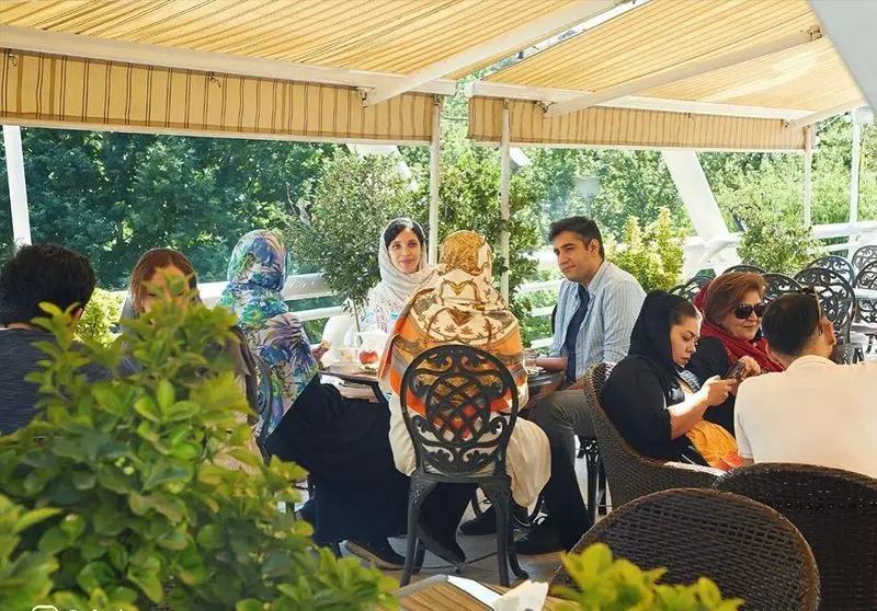 جمعی از مشتریان در فضای باز و سرسبز کافه شمرون تهران، در حال گپ و گفت و لذت بردن از نوشیدنی‌ها در یک روز دلنشین.