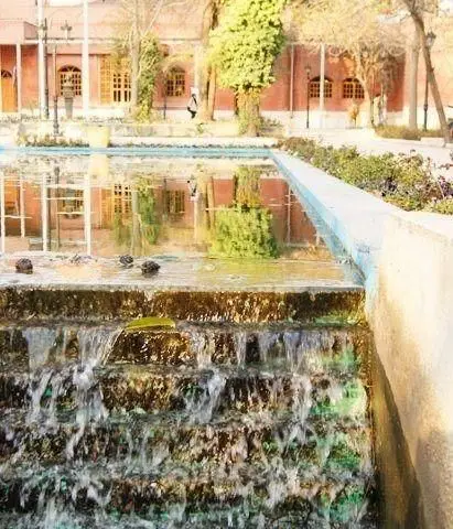 نمای زیبا از سفره خانه سنتی انارستان، با آبشار پلکانی، حوض آب و بازتاب ساختمان آجری در آن، فضایی دلنشین و آرامبخش.