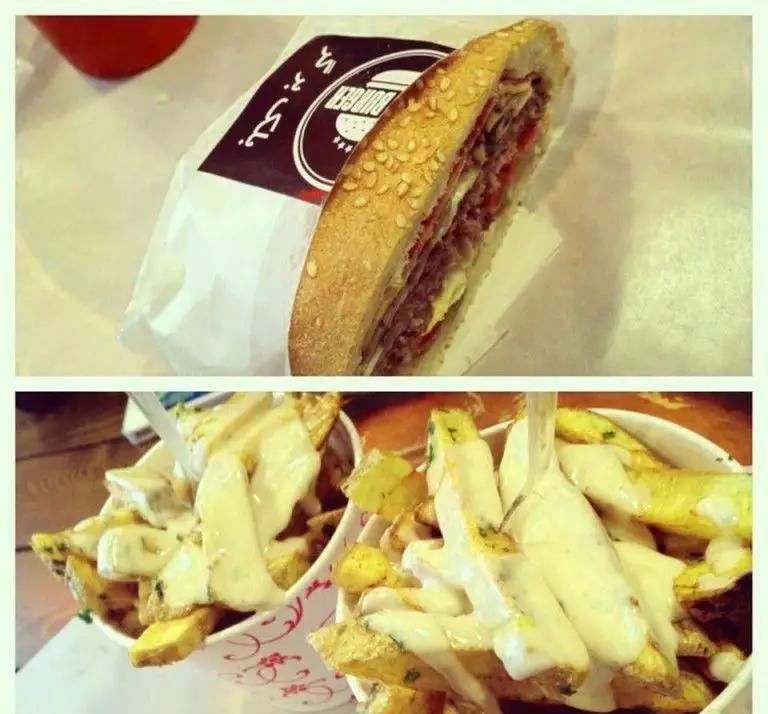 نمایی از ساندویچ دلپذیر بلک برگر با نان کنجدی و دو ظرف سیب‌زمینی سرخ شده با سس سفید و سبزی، انتخابی عالی از فست فود بلک برگر.