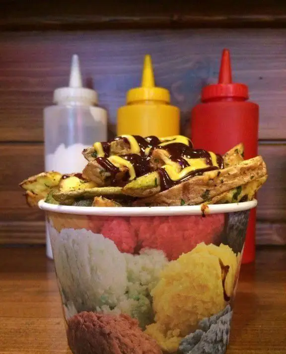 وافل سیب‌زمینی خوشمزه بلک برگر با سس پنیر و سس باربیکیو غلیظ، در لیوانی طرح‌دار با پس‌زمینه بطری‌های کچاپ، خردل و مایونز.