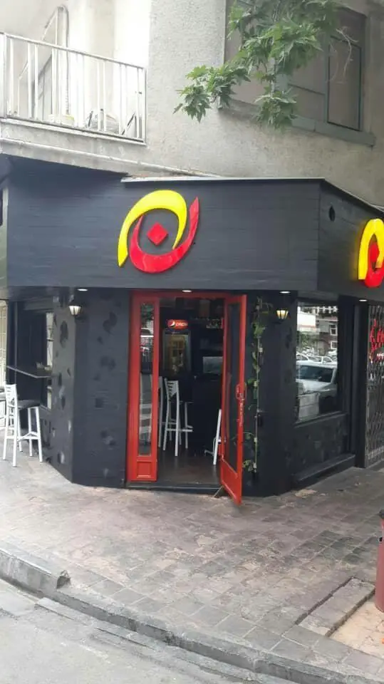 تصویری از نمای بیرونی کافه برگر ن با دکوراسیون شیک مشکی، درب قرمز ورودی و لوگوی جذاب زرد و قرمز، فضایی دلنشین برای مشتریان.