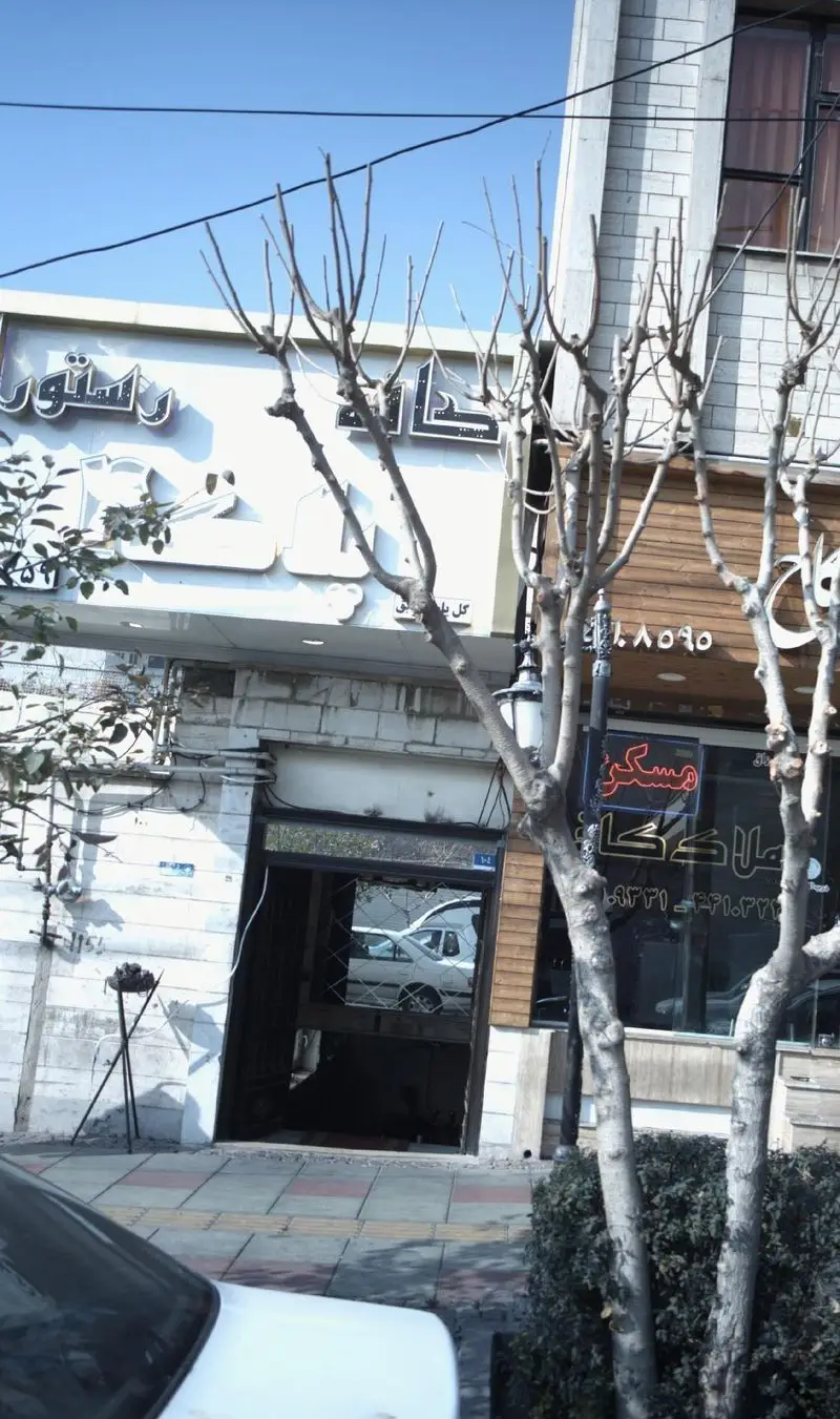 تصویری از نمای بیرونی رستوران پلاک 4 در خیابان، با تابلوی کسب و کار، درختان بدون برگ و ساختمان‌های اطراف در یک روز آفتابی.