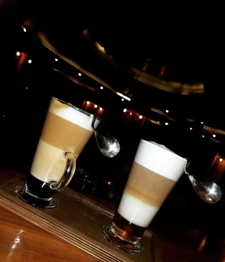 دو لیوان لاته ماکیاتو خوش‌رنگ و لایه‌ای در فضای دنج و شبانه کافه دایموند، مناسب برای لحظاتی دلنشین و آرامش‌بخش.