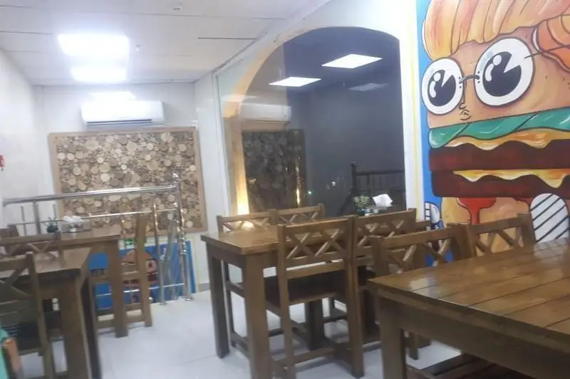 فضای داخلی دنج و مدرن فست فود ممدخان با میز و صندلی‌های چوبی، دیوارنگاری بزرگ برگر، و دکوراسیون هنری چوبی.