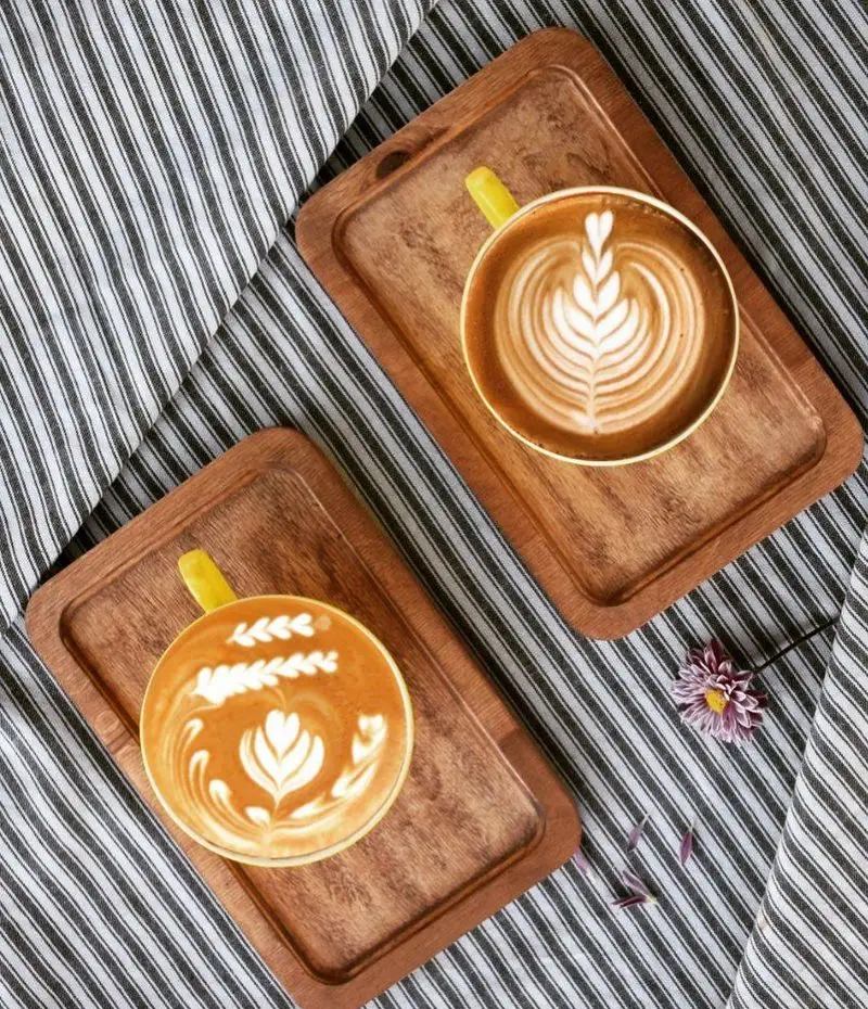 دو فنجان قهوه با لاته آرت زیبا روی سینی‌های چوبی در کافه دارچینی. منظره‌ای دلنشین برای شروع روز با نوشیدنی‌های گرم.
