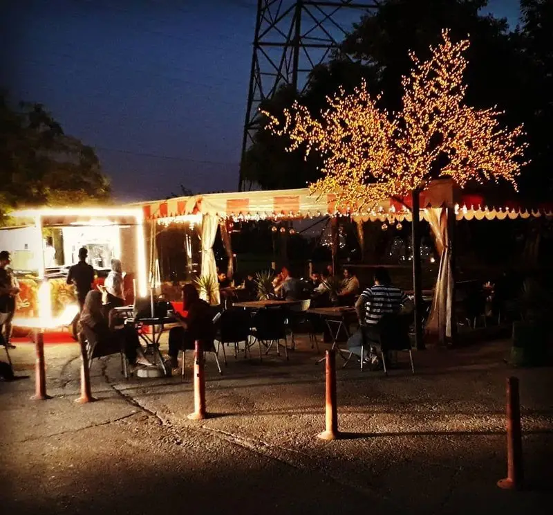 تجربه شب‌نشینی بی‌نظیر در کافه دارچینی: فضای باز با نورپردازی خاص و درخت نورانی، محلی دنج برای لذت از غذا و نوشیدنی.