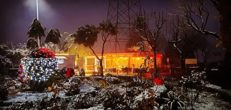 کافه دارچینی در شبی برفی و زیبا، با نورپردازی گرم و چراغانی دلنشین، فضایی دنج و رمانتیک برای زمستان ایجاد کرده است.