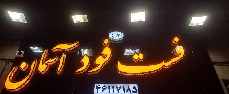 تابلوی نئون درخشان فست فود آسمان با نور نارنجی، شامل لوگوی «هو الرزاق» و شماره تماس 46117185 برای شناسایی بهتر کسب و کار