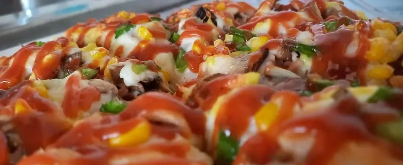 یک برش نزدیک و اشتهاآور از پیتزا مخصوص فست فود آسمان با ترکیبی از پنیر، گوشت، ذرت، فلفل دلمه و سس خوش‌طعم.