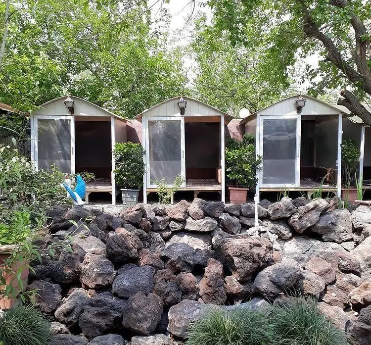 نمایی از آلاچیق‌های اختصاصی باغ رستوران برکه؛ فضاهایی دنج با دیوارهای سنگی، درختان سرسبز و محیطی آرامش‌بخش.