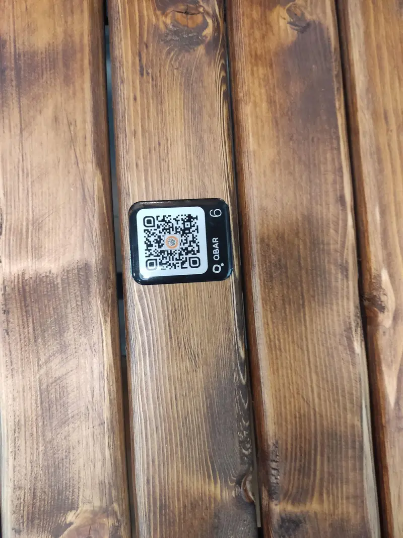 کد QR مخصوص کافه ترنج بر روی میز چوبی با لوگوی QBAR و شماره ۶ برای دسترسی سریع به منو و سفارش آنلاین.