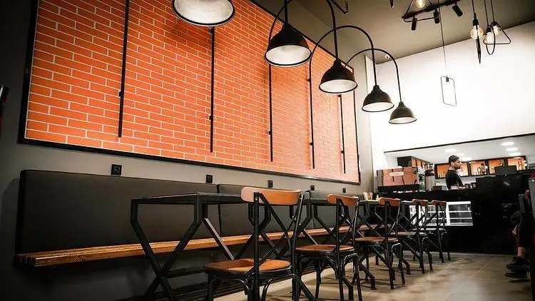 دکوراسیون داخلی مدرن و صنعتی کافه ترنج با دیوار آجری و نورپردازی زیبا، همراه با چیدمان میز و صندلی‌های شیک و پیشخوان فعال قهوه
