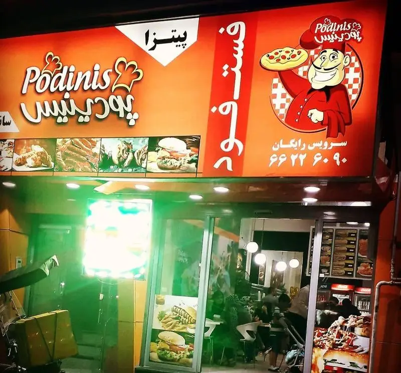 تصویری از نمای بیرونی فست فود پودینیس در شب با تابلوی روشن، شامل لوگو، یک سرآشپز با پیتزا و انواع غذاهای لذیذ مانند برگر و ساندویچ.