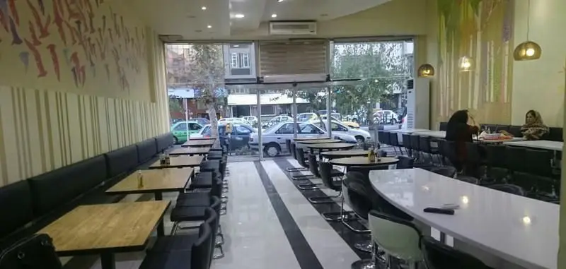 فضای داخلی دنج و مدرن فست فود تومس با چیدمان میز و صندلی‌های راحت، دیوارنگاره‌های جذاب و منظره خیابان از پنجره‌ها.