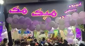 نمای شلوغ و جشن‌مانند از مغازه آبمیوه و بستنی میک مک با بادکنک‌های بنفش و سفید و مشتریان در حال لذت بردن از نوشیدنی‌ها و دسرها.