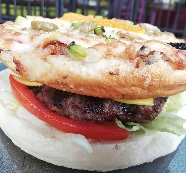 تصویر نزدیک از همبرگر ویژه فست فود گاراژ با نان پیتزایی مزین به قارچ، فلفل و ذرت، شامل پنیر، پتی گوشت و سبزیجات تازه.