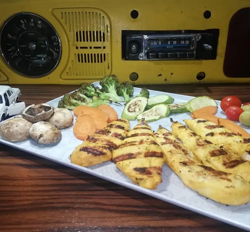 سینه مرغ گریل شده و سالم با بروکلی، هویج، کدو و قارچ در فست فود گاراژ، در فضایی با تم خودرویی نوستالژیک.