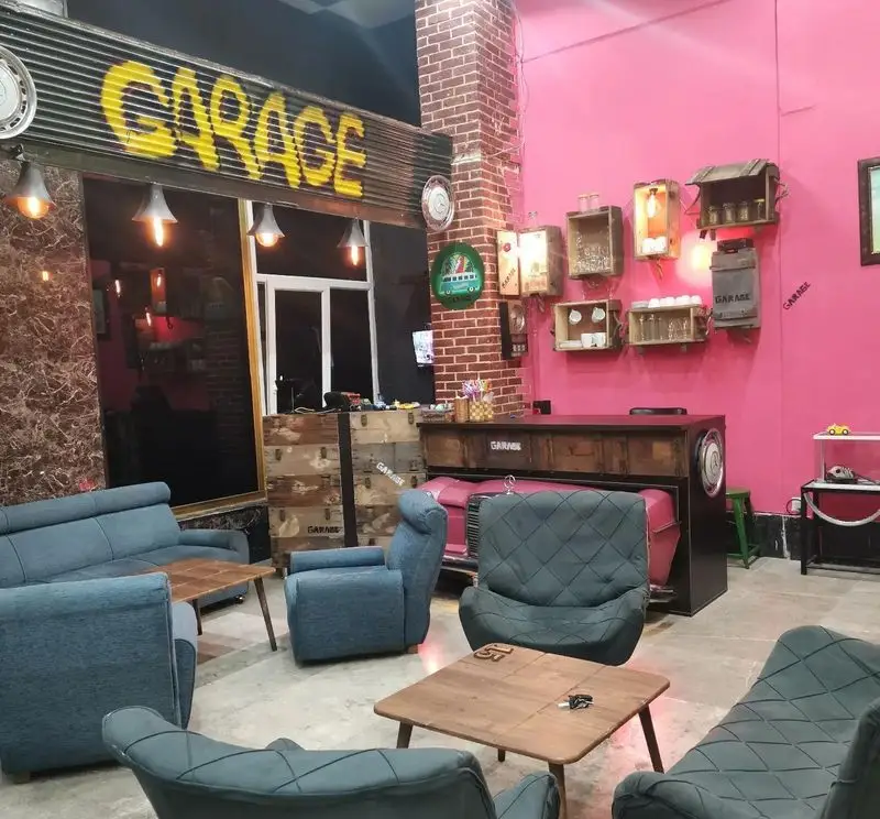 دکوراسیون داخلی فست فود گاراژ، فضایی صنعتی و مدرن با دیوار صورتی، مبلمان راحتی، میزهای چوبی و تابلوی "GARAGE" برای تجربه‌ای دلنشین.