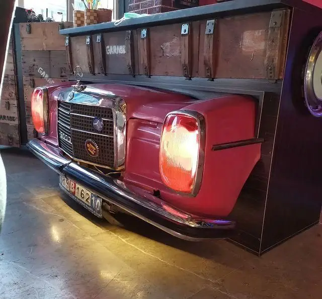 تصویری از دکوراسیون داخلی فست فود گاراژ؛ پیشخوانی خاص با جلوی ماشین کلاسیک مرسدس بنز صورتی و المان‌های گاراژی.