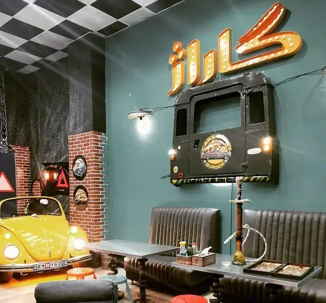 فضای داخلی و دکوراسیون منحصربفرد فست فود گاراژ با تم خودرویی. شامل فولکس واگن زرد، جلوپنجره ماشین و تابلوی نئون "کاراژ" بالای صندلی‌های چرمی.