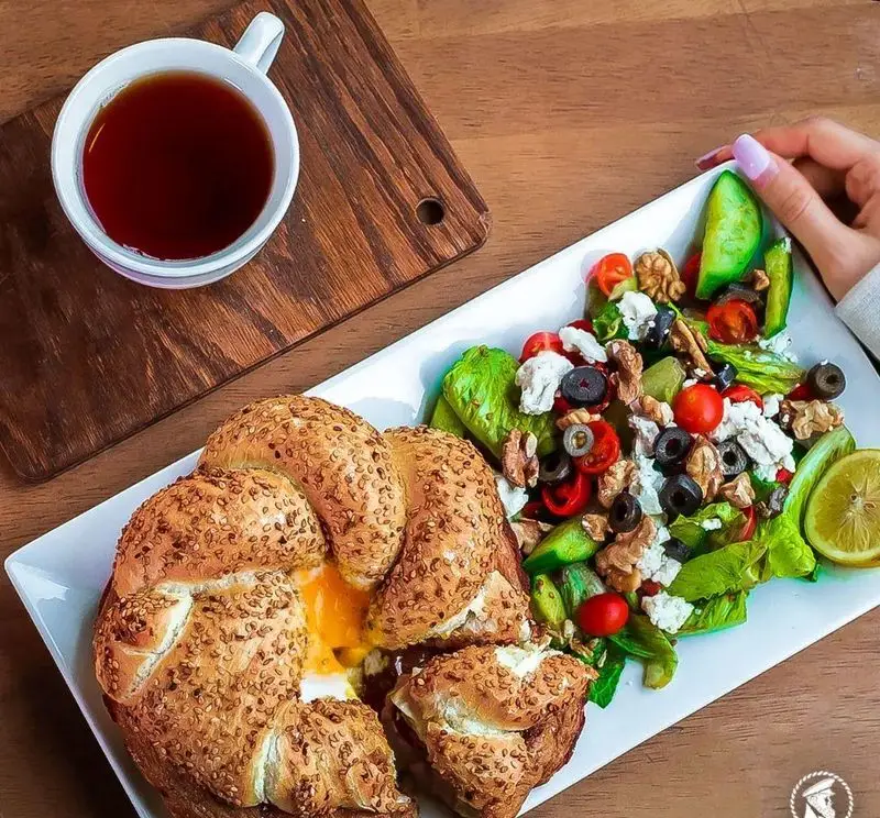 صبحانه کامل و دلپذیر شامل نان کنجدی با تخم مرغ، سالاد تازه با پنیر، زیتون و گردو، همراه با چای داغ در کافی شاپ کاپیتان لانژ.