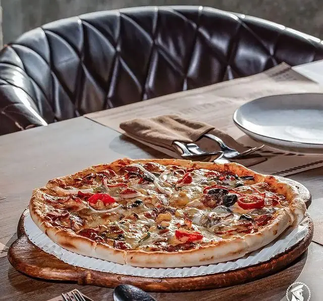 پیتزای خوشمزه و داغ روی میز چوبی در کافی شاپ کاپیتان لانژ، با صندلی چرمی لوکس و چیدمان شیک رستوران.
