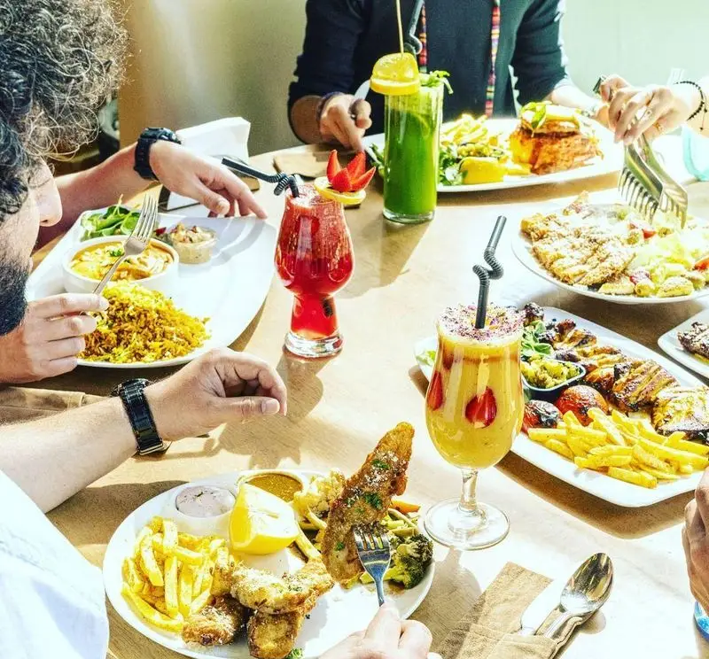 تجربه غذایی دلنشین در کافی شاپ و رستوران کاپیتان لانژ با میز پر از غذاهای لذیذ، از ماهی و برنج تا مرغ و سالاد و نوشیدنی‌های جذاب.