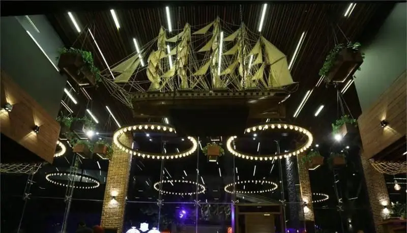 دکوراسیون داخلی کافی شاپ کاپیتان لانژ با کشتی بزرگ معلق، نورپردازی خیره کننده، لوسترهای مدرن و فضایی لوکس و دلنشین.