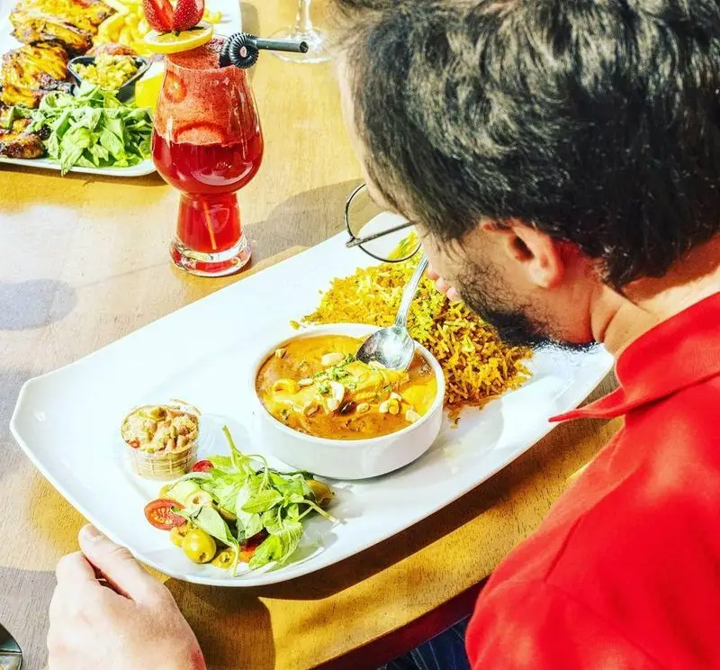 تجربه دلنشین مشتری در کافی شاپ کاپیتان لانژ با سرو غذای ویژه شامل مرغ کاری، برنج زعفرانی، سالاد تازه و نوشیدنی خنک در فضایی دنج و شیک.