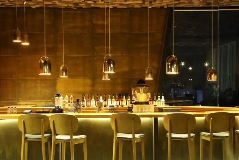 تصویری از دکوراسیون داخلی شیک و مدرن کافی شاپ کاپیتان لانژ با میز بار طلایی، صندلی‌های چوبی و نورپردازی گرم و دلنشین.