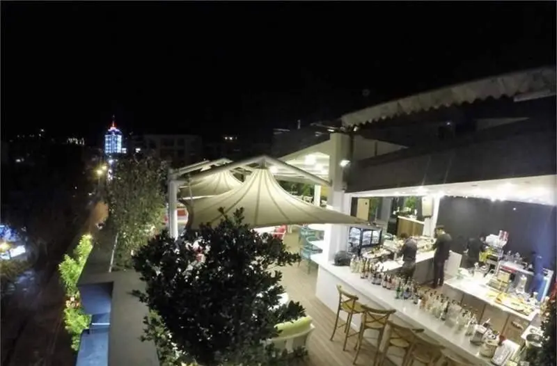 کافی شاپ کاپیتان لانژ: چشم‌انداز شبانه دلنشین از فضای باز کافه با سایبان‌های مدرن، میز بار پرنور و نمایی از شهر.