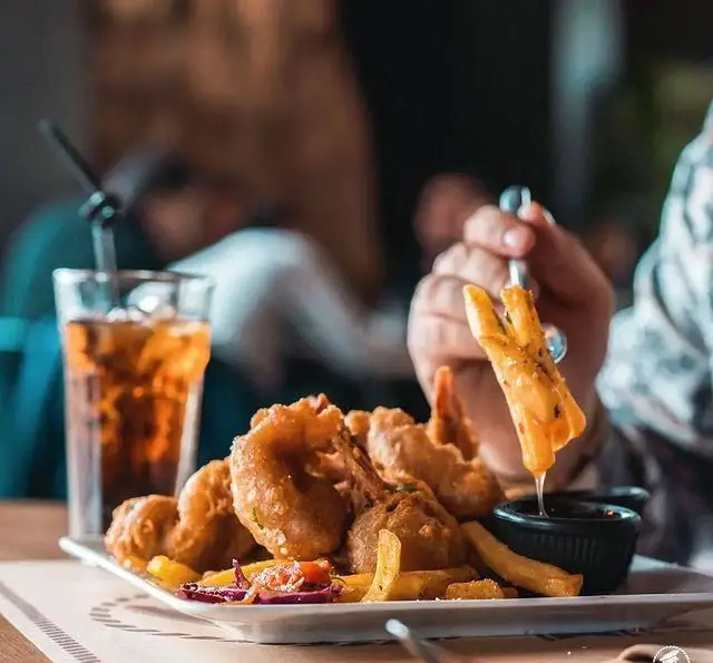 تجربه لذت‌بخش یک مشتری در کافی شاپ کاپیتان لانژ: غذای سوخاری، سیب‌زمینی سرخ کرده و نوشیدنی خنک در فضایی دلپذیر.