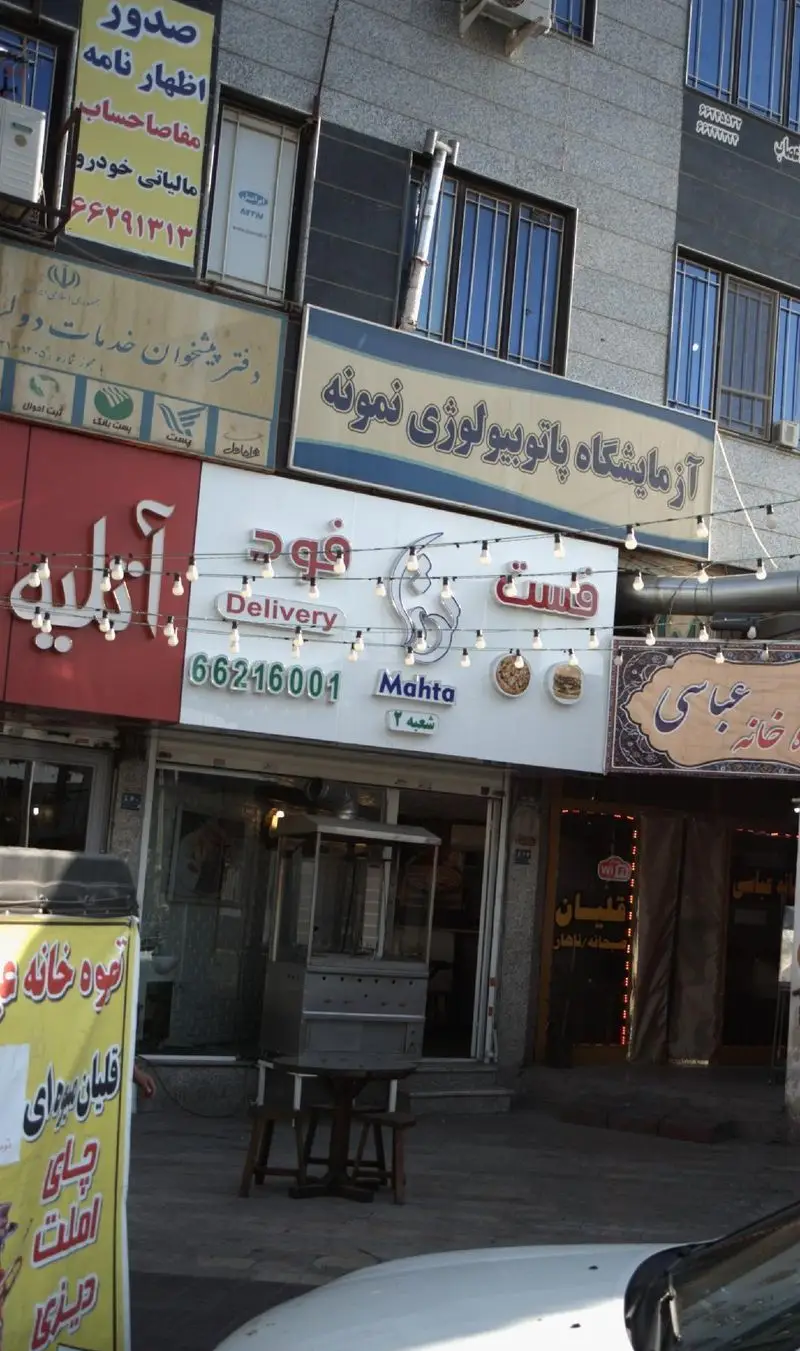 نمای نزدیک از تابلوی فست فود مهتا با کلمه Delivery، شماره تلفن 66216001، و اشاره به شعبه 2 در خیابان.