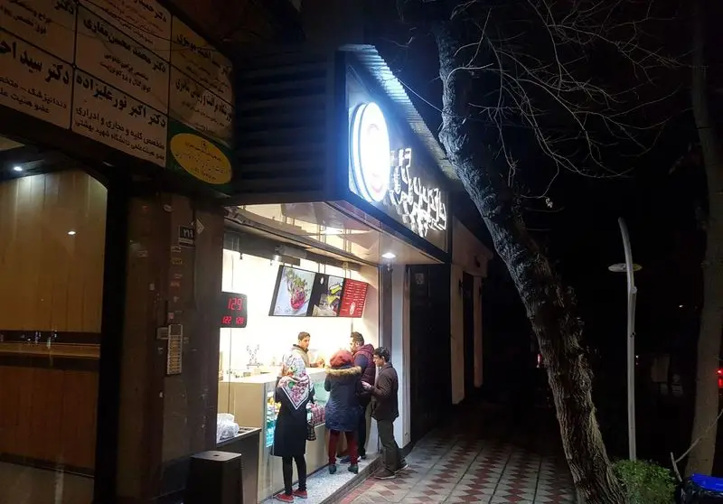 تصویری جذاب از نمای بیرونی هاکوپ برگر در شب با نورپردازی روشن و مشتریانی که برای برگر و فست فود صف کشیده‌اند.