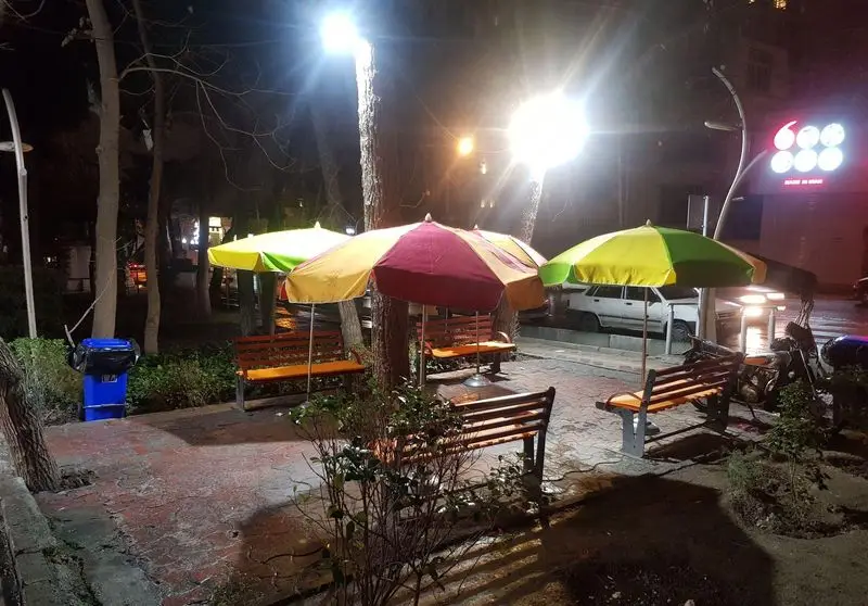 نمایی از فضای باز رستوران هاکوپ برگر در شب با نورپردازی، شامل نیمکت‌های راحت و چترهای رنگارنگ آماده پذیرایی از مشتریان.